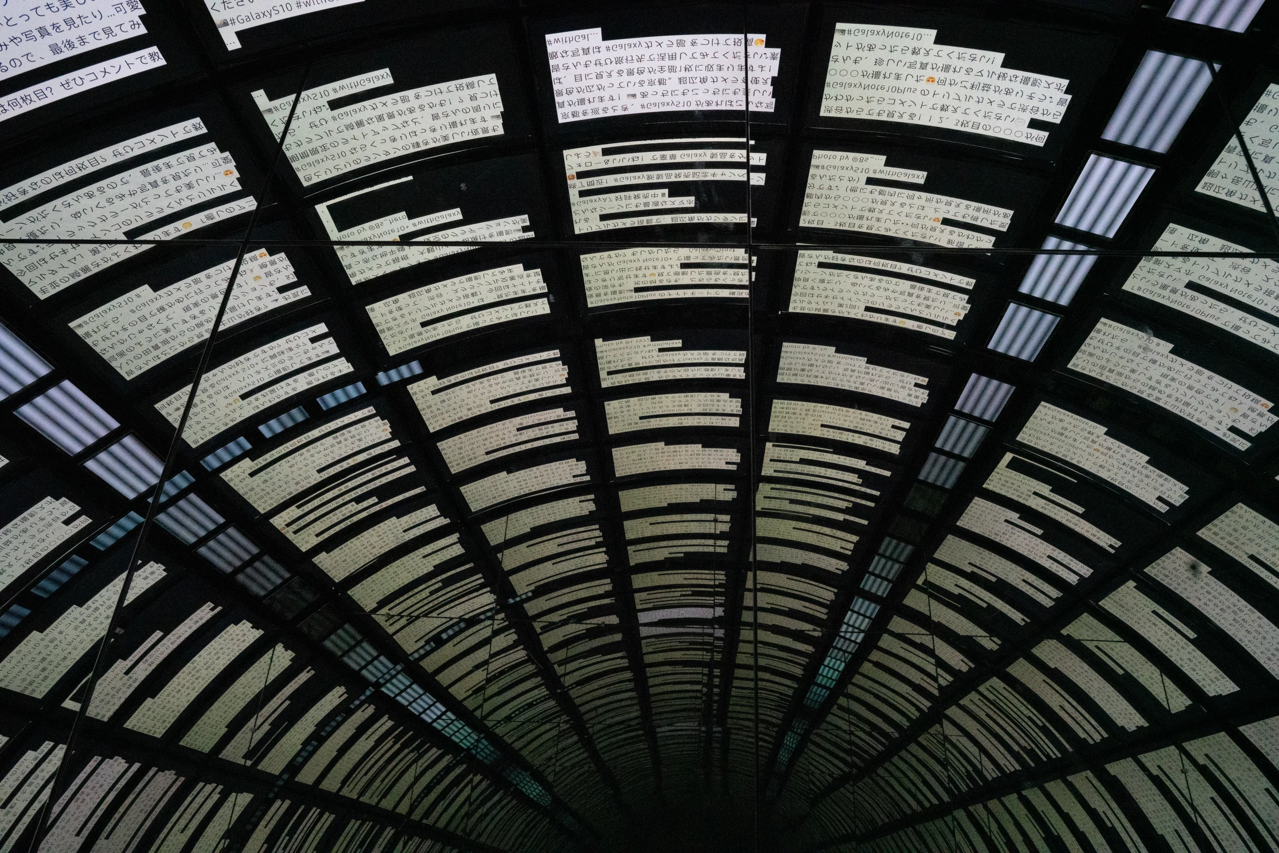 A curved glass-and-metal arcade roof seen from below in repeating dark bands.