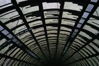 A curved glass-and-metal arcade roof seen from below in repeating dark bands.