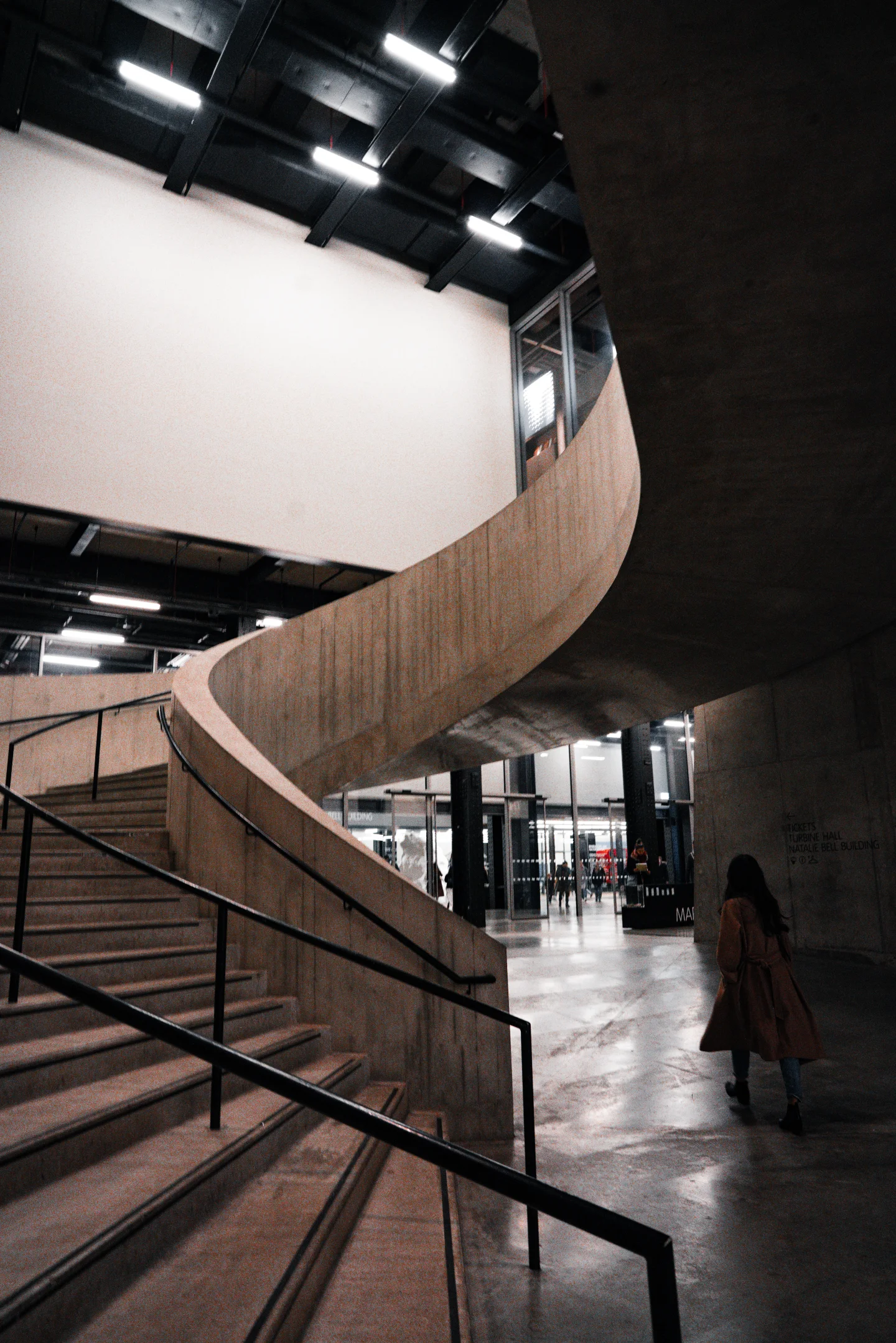A sweeping concrete stair curls through a modern interior under bright strip lighting.