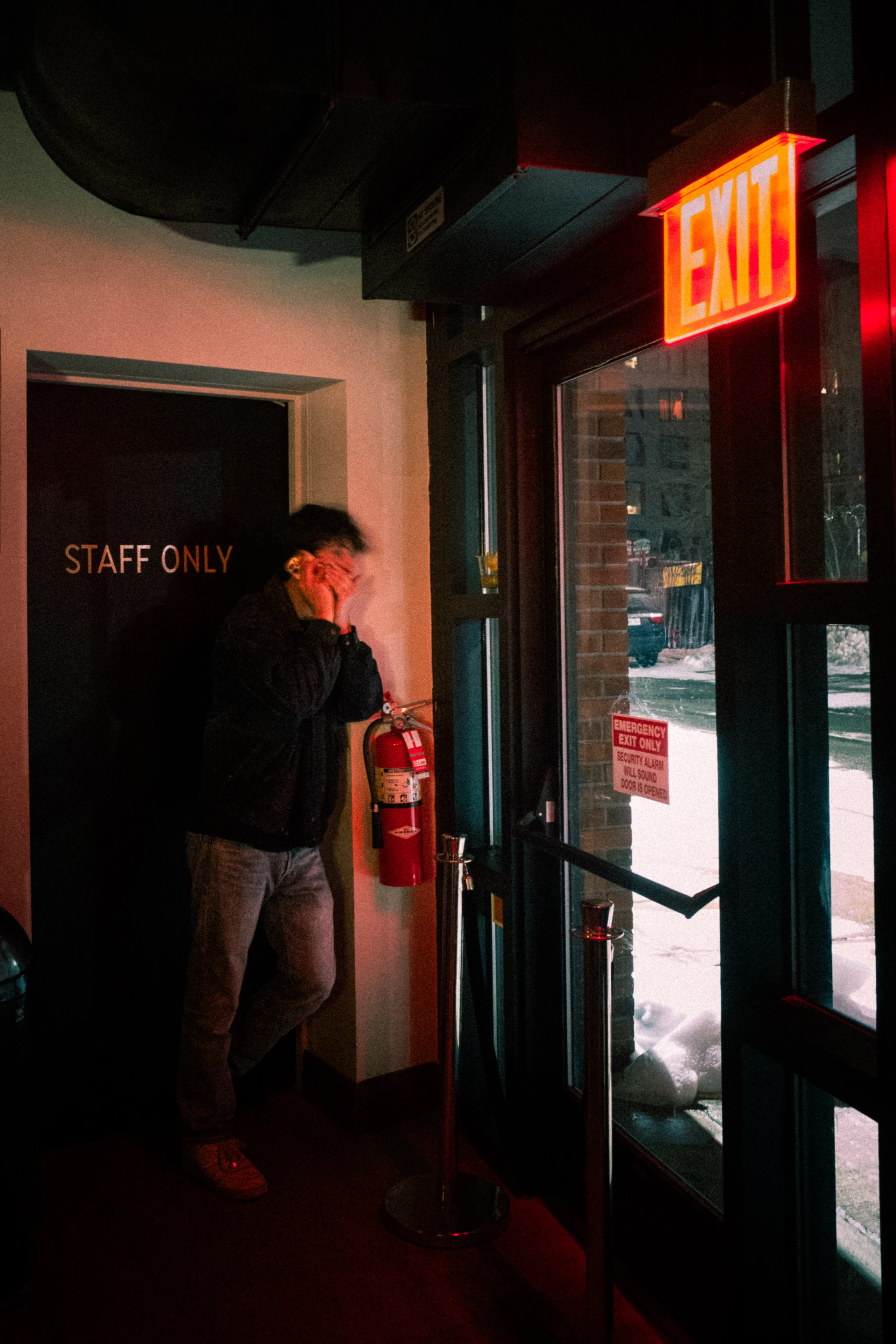 A man stands beneath a red exit sign at a staff-only bar doorway.