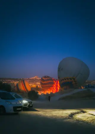 Vehicles and a large balloon on a field before dawn.