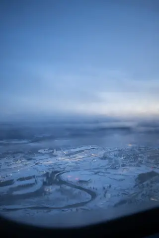 A snow-covered Fairbanks neighborhood and roads seen from an airplane through low blue cloud.