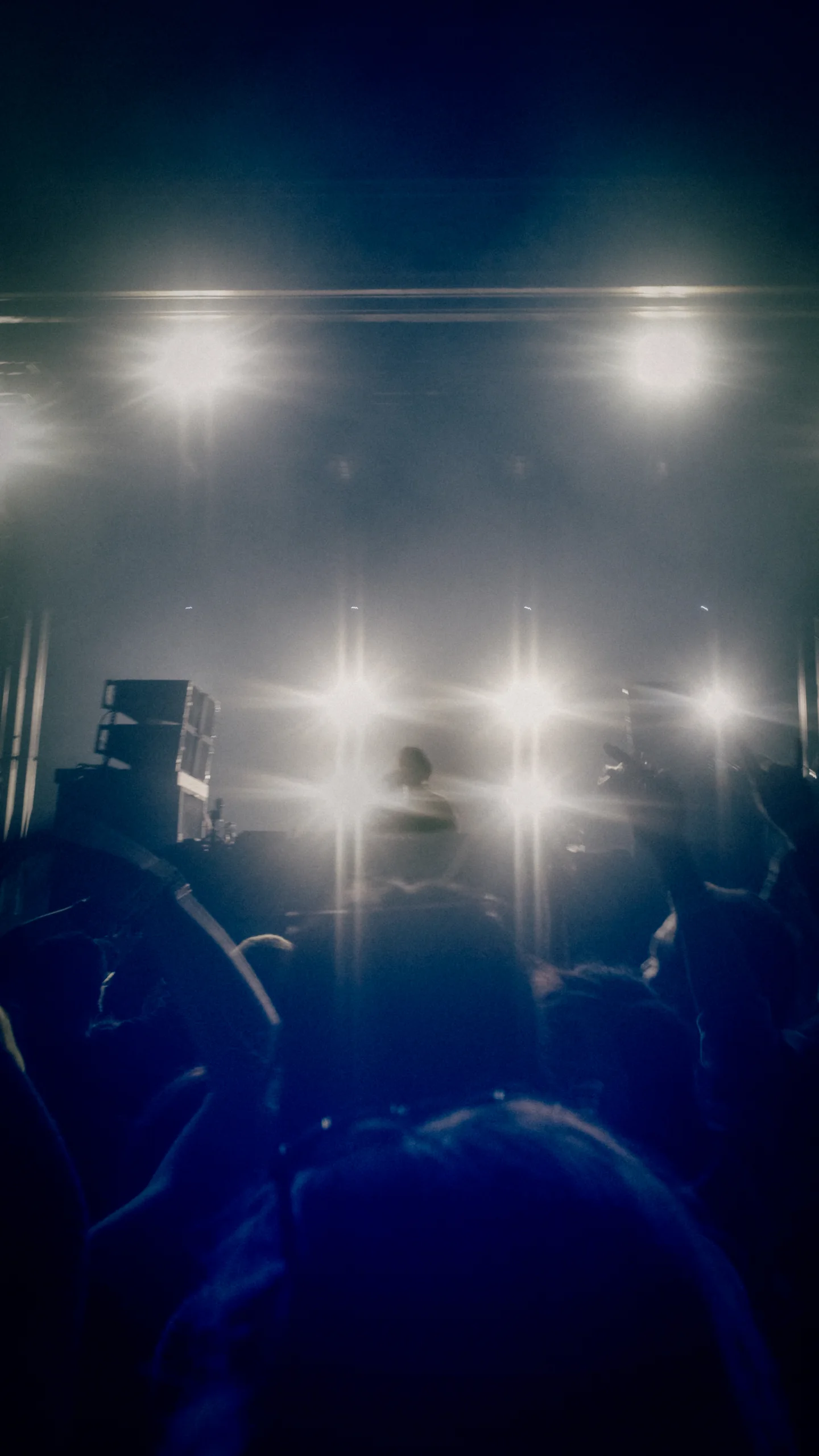 Silhouetted crowd and performers against a wall of bright white stage lights in blue haze.