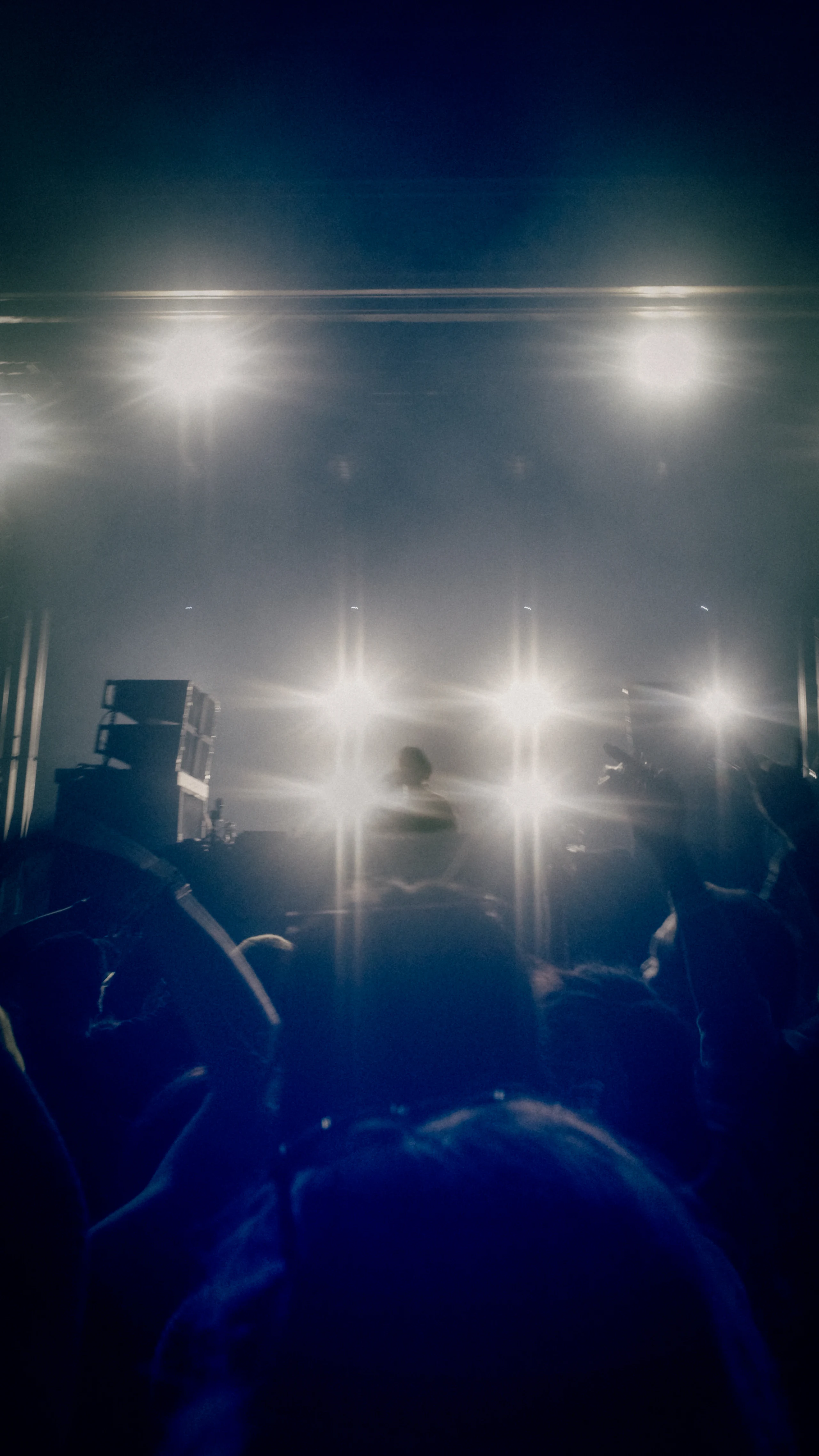 Silhouetted crowd and performers against a wall of bright white stage lights in blue haze.