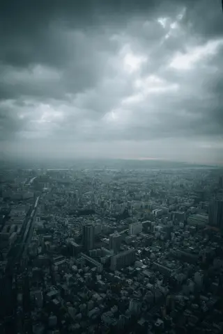 A broad Tokyo skyline viewed from above beneath dramatic gray clouds.