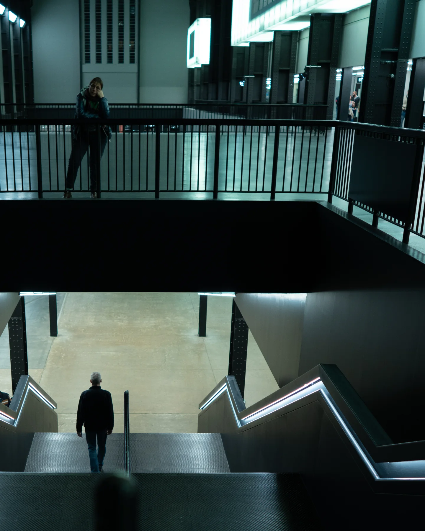 People standing on upper and lower walkways inside a geometric concrete interior.