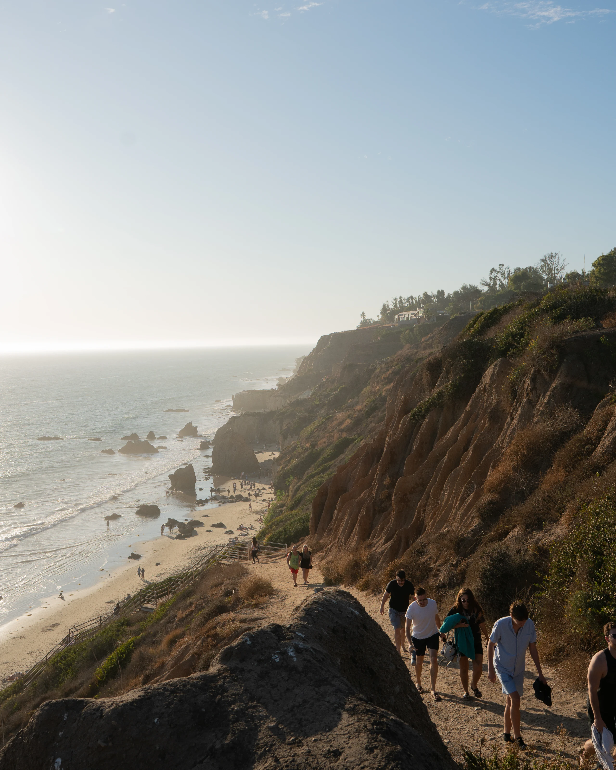Hikers walking a cliffside trail above the coast.