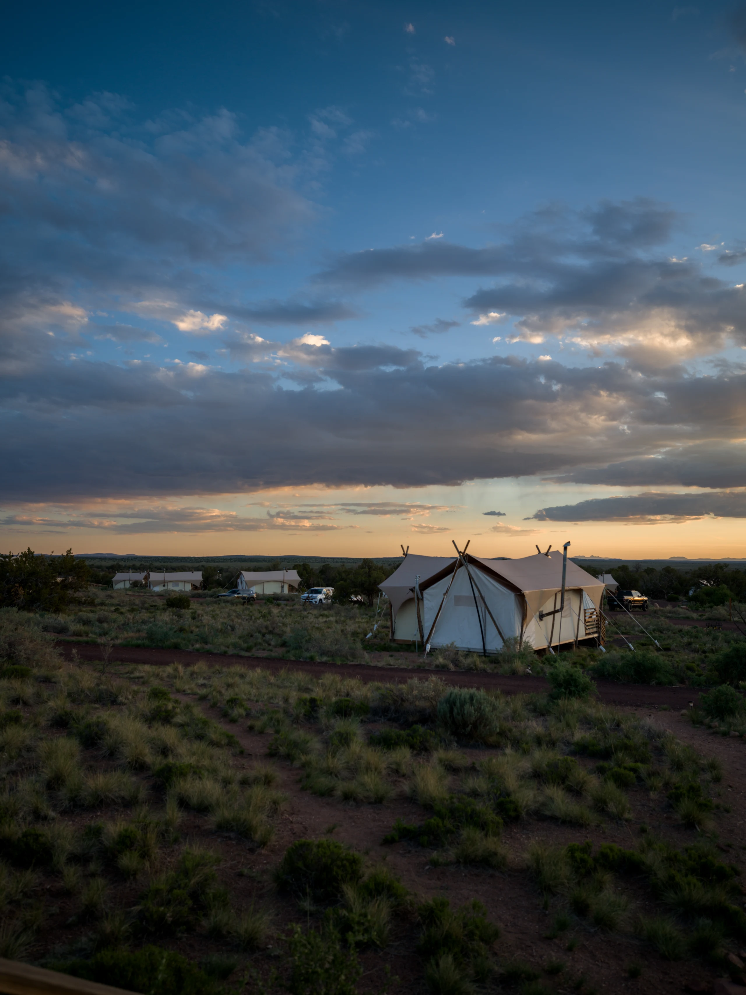 A white tent stands alone in desert scrub beneath evening clouds.