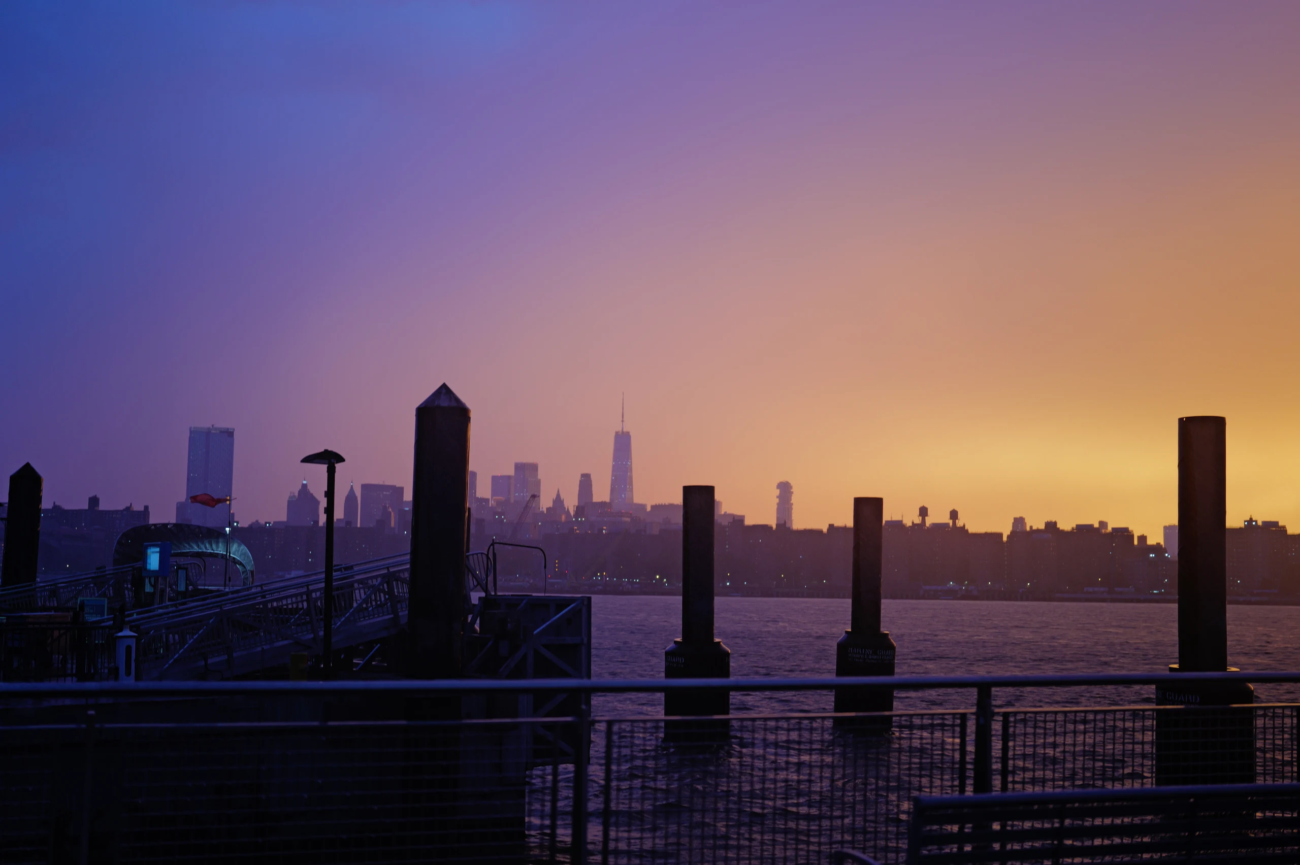 The Manhattan skyline across the East River beneath a violet and orange sunset.