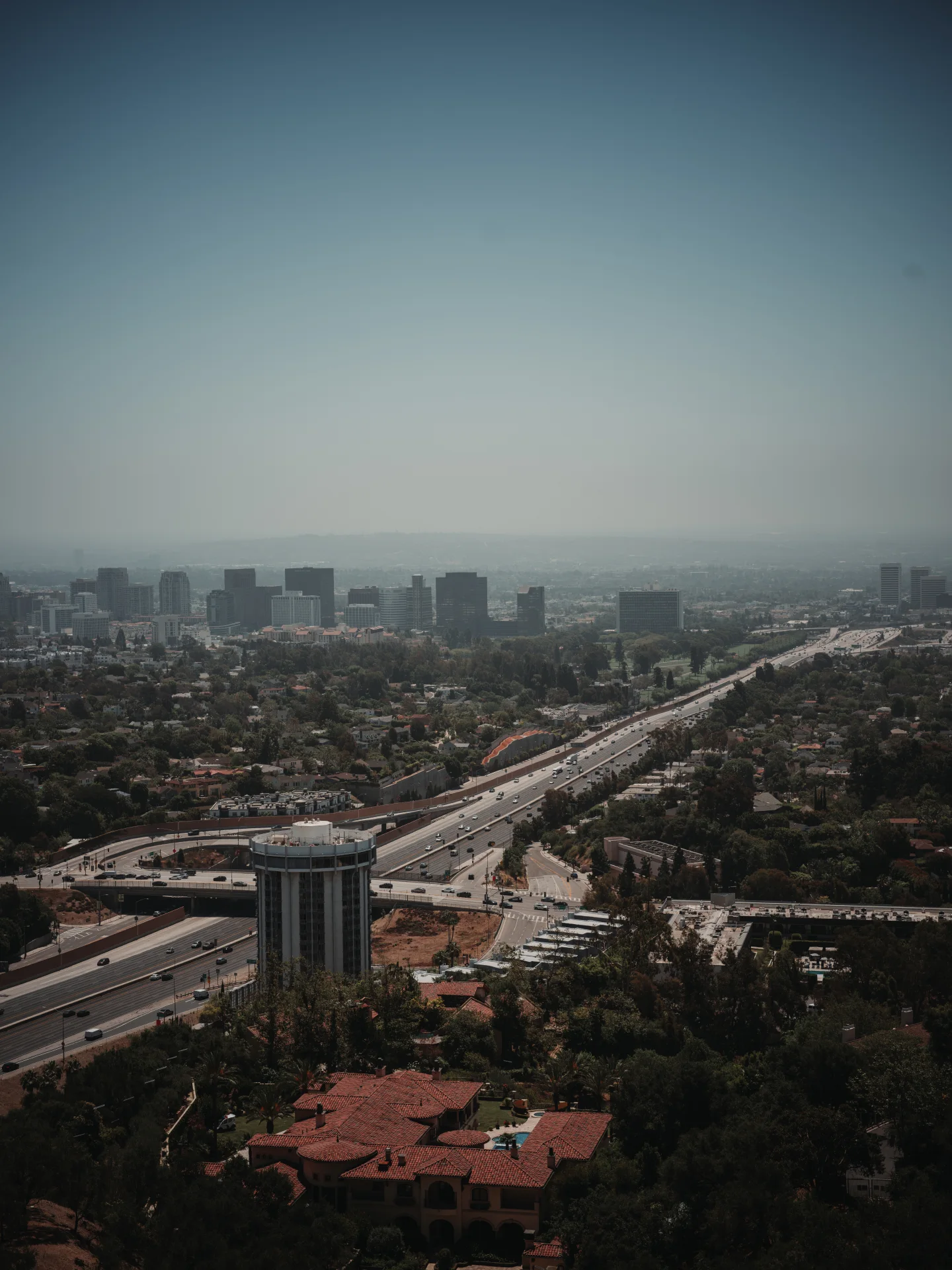Wide elevated view of Los Angeles neighborhoods and freeway beneath a hazy sky