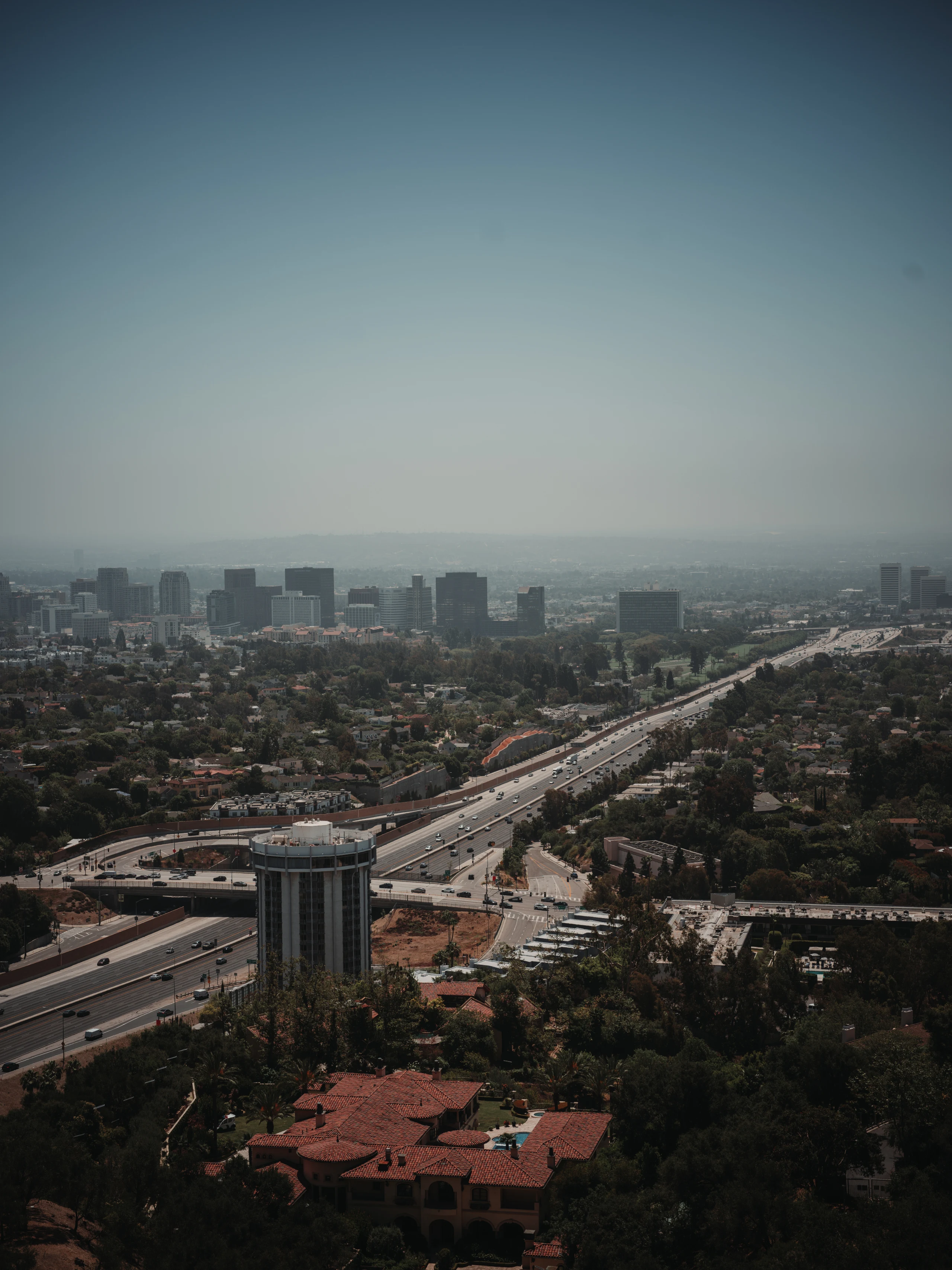Wide elevated view of Los Angeles neighborhoods and freeway beneath a hazy sky