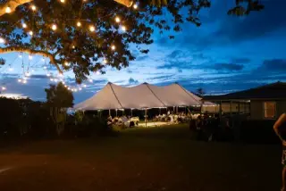 Wedding reception tent glowing at dusk beneath string lights.