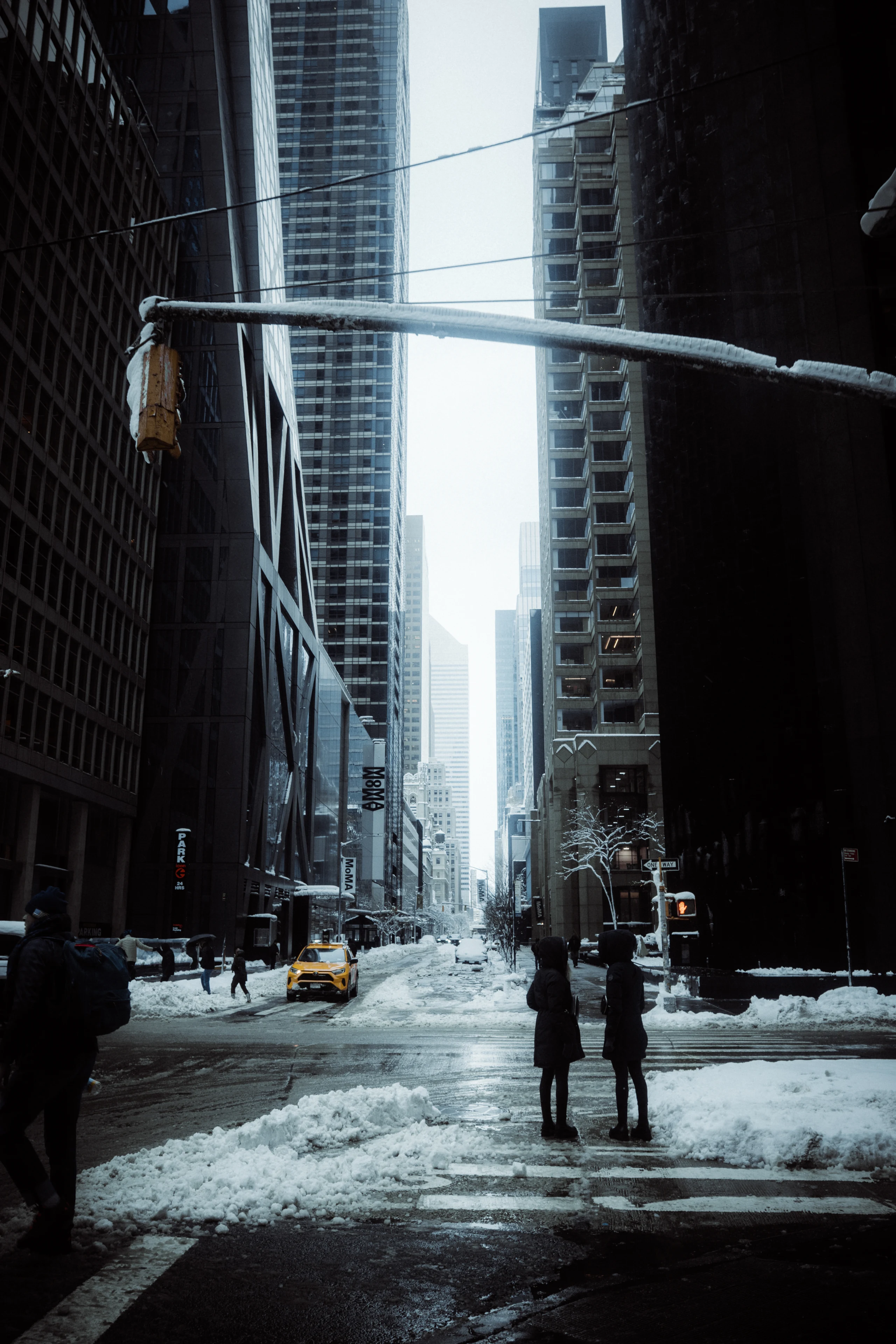 Two people waiting at a Midtown crosswalk surrounded by snow