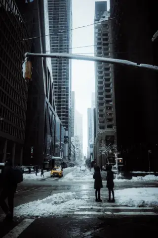 Two people waiting at a Midtown crosswalk surrounded by snow