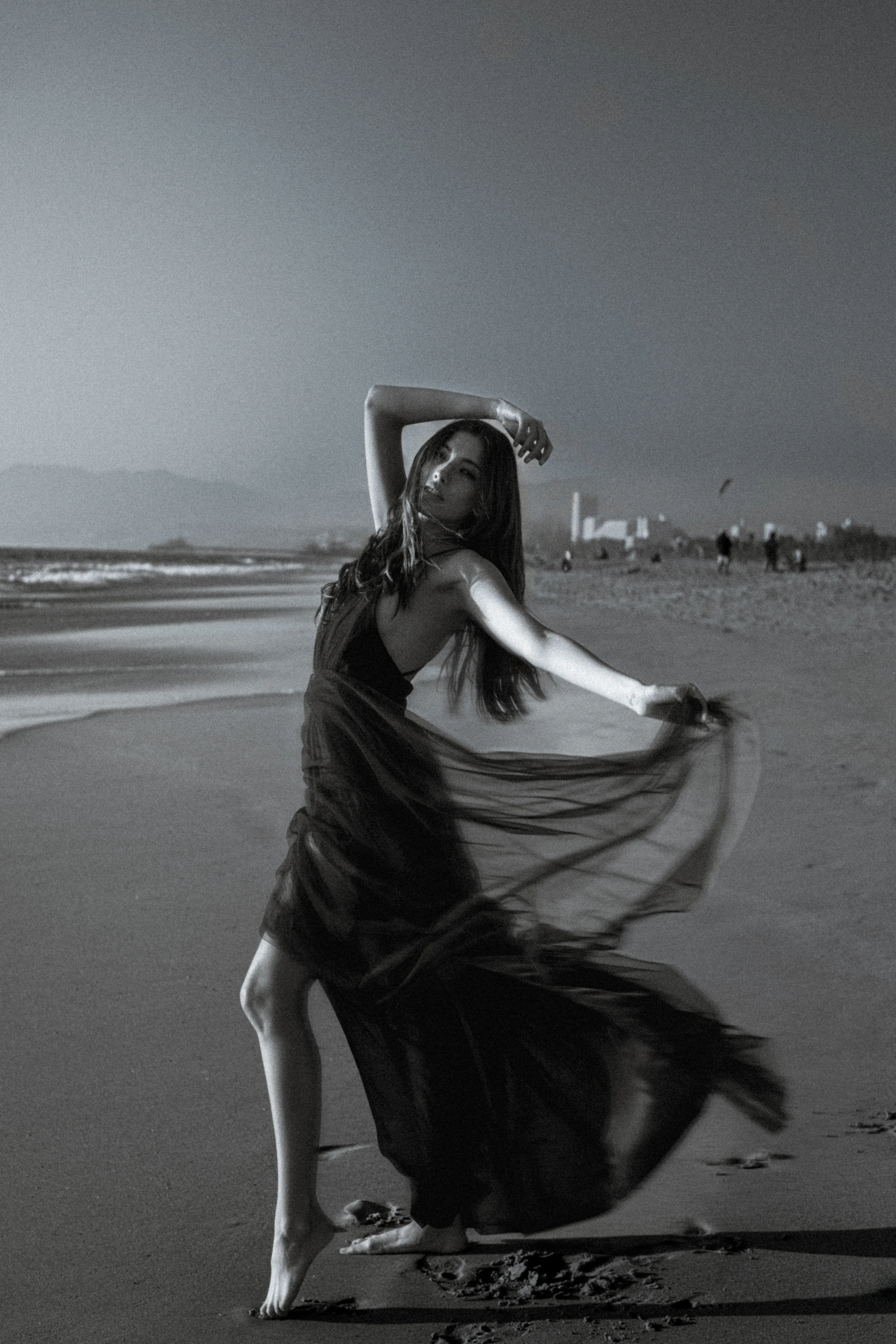 Woman posing with a flowing dress on a beach in black and white.